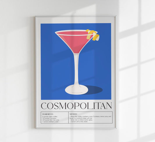 A framed poster of a Cosmopolitan drink with a blue background, featuring a glass of pink liquid with a lemon garnish on a white wall.