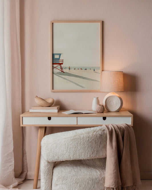 Nestled corner with a wooden desk against a pink wall, featuring a framed beach scene, lamp, and decorative items.